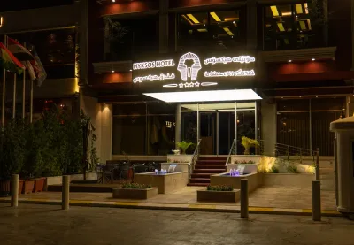 دیمەنی پێشەوەی Hyksos Hotel بە تابلۆی سێزمانی ڕووناککراوە لە شەودا